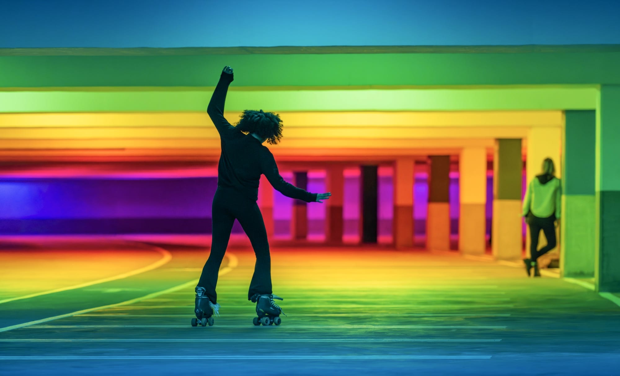 A man roller skates through a parking garage lit by colorful lights in an art installation by Liz West